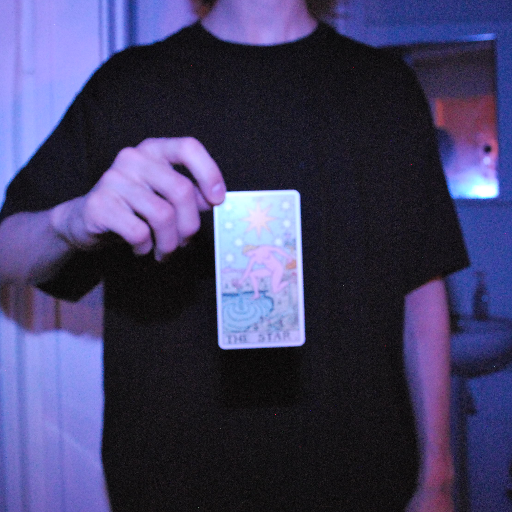 a person holding the tarot card 'the star' lit by a blue light