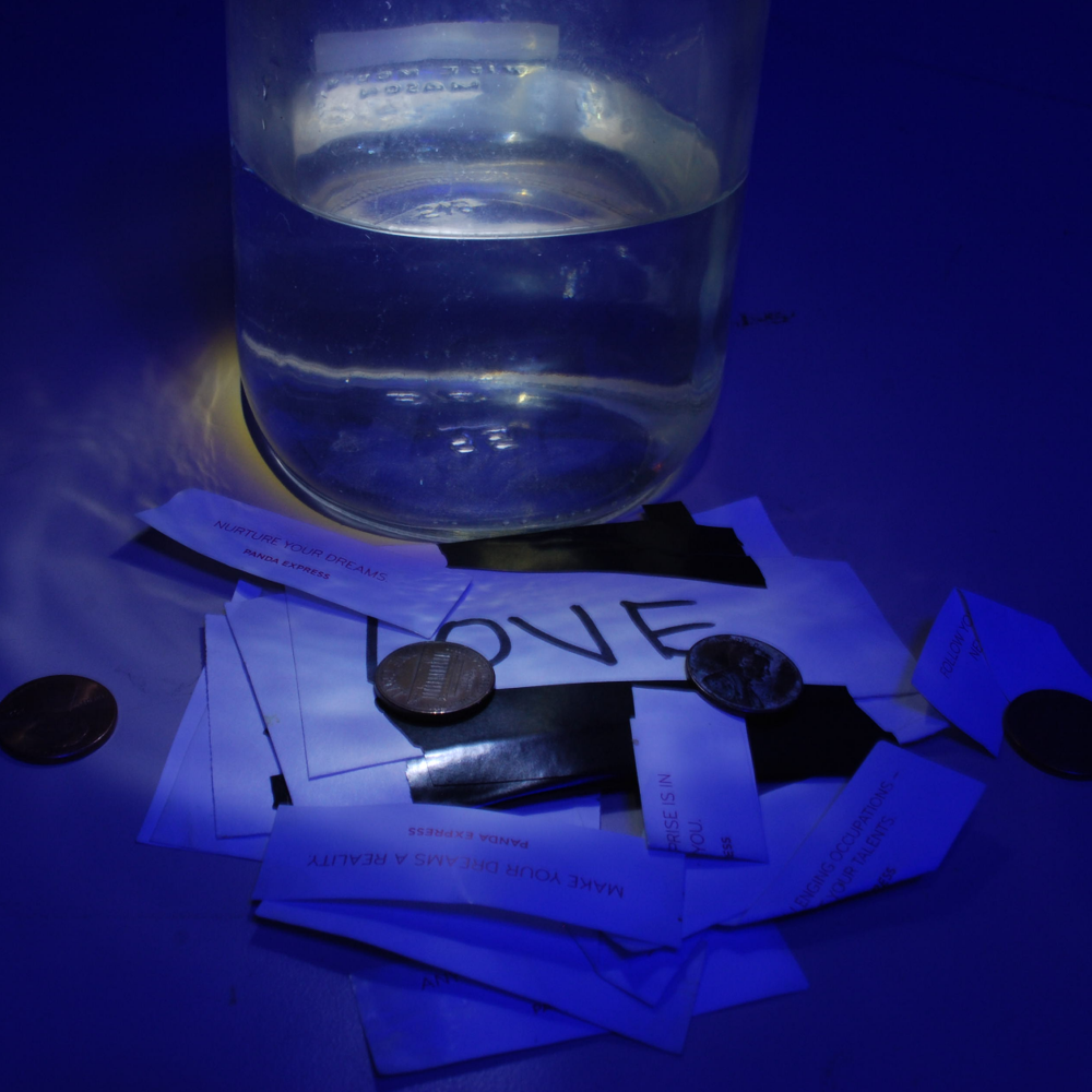 image of a jar of water with a white light shining on it, surrounded by four coins and papers draped in blue light