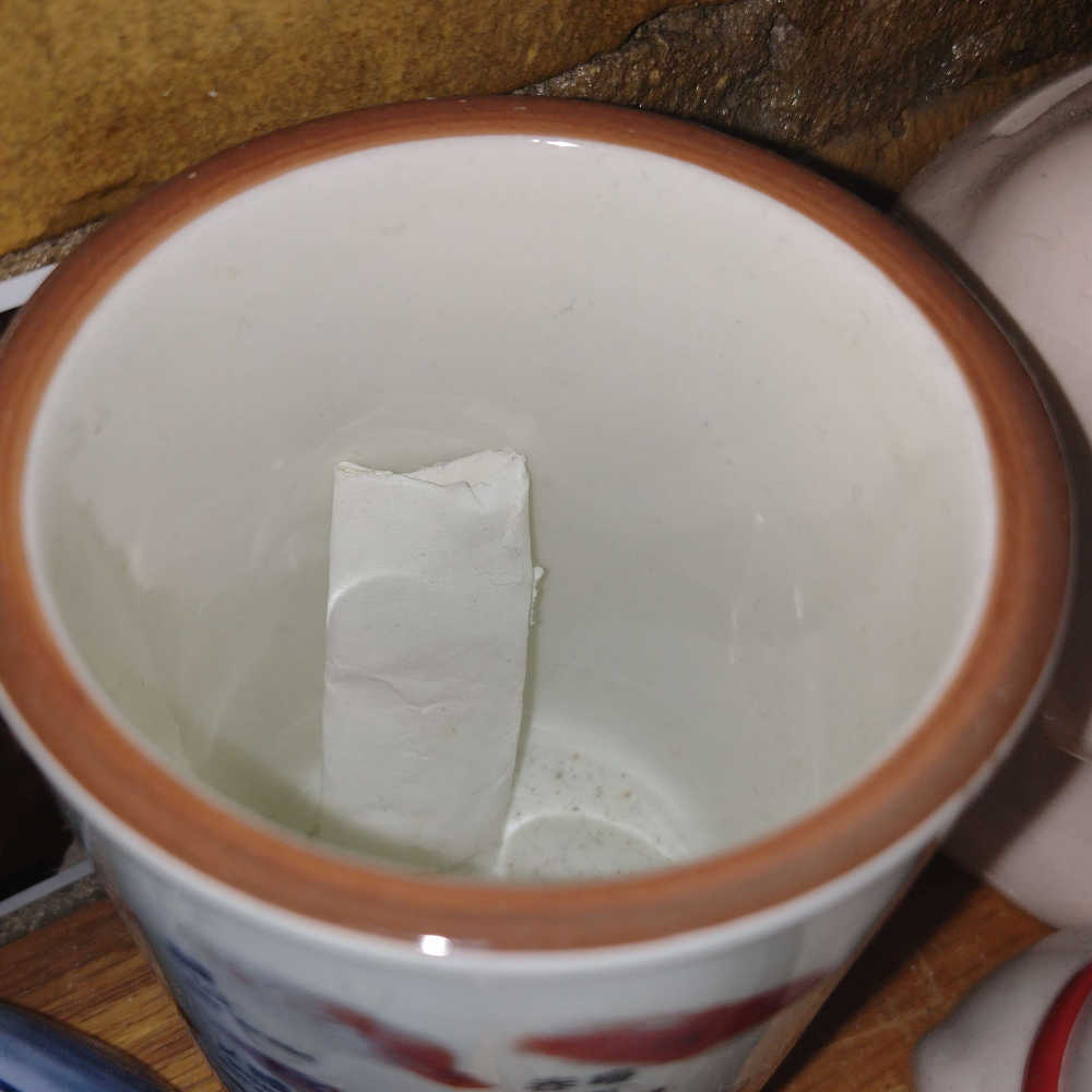 a piece of folded paper in a porcelain cup with a brick wall in the back